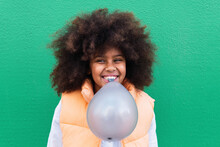Happy Girl Holding Balloon In Mouth Against Green Background
