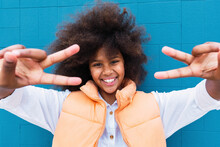 Smiling Girl Gesturing Peace Sign In Front Of Blue Wall