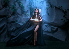 Fairy Woman Elf Queen In Black Fantasy Sexy Long Dress Fly In Wind Cape Flutter Waving Flowing Around Witch Princess Goth Girl Sharp Ears Golden Crown. Old Style Cave. Spell Light In Hand Dark Magic 