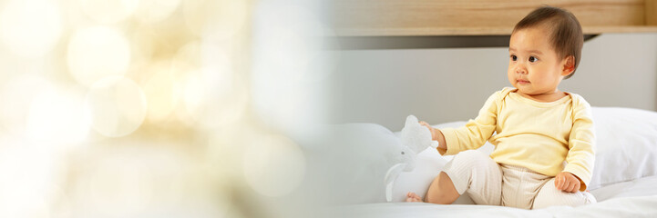 Asian baby girl with white skin and big eyes  naughty age  playing on the bed by the bedroom window web banner with copy space on left