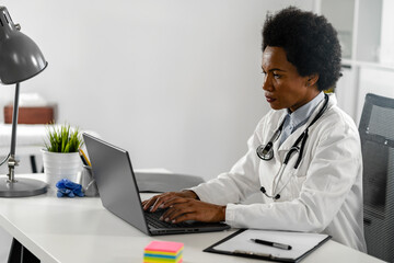 Wall Mural - Female doctor working at her office in front of laptop computer, writing a health report