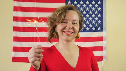 Wall Mural - A woman in a red sweatshirt waves sparklers against the background of the US flag. Slow motion portrait. Independence Day. USA day