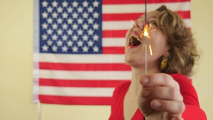 Wall Mural - Cheerful portrait of a woman with sparklers on the background of the USA flag. American woman. Woman in a red sweater. Slow motion 4k