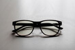 Defocus black eyeglasses on white background. Flat lay, top view. A pair of dark-rimmed glasses viewed from the front, with the temples open. The background is white. Out of focus
