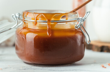 Wall Mural - Glass jar of brown salted caramel with smudges and a wooden spoon inside on a white background