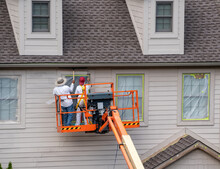 Two Home Painters In Articulating Boom Lift Spray Painting Townhouse