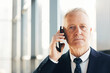 © Mediaphotos - Portrait of serious displeased mature businessman with wrinkled face standing in office hall and answering call by mobile phone