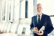 © Mediaphotos - Portrait of serious confident senior executive in dark formal suit standing in conference room and making notes in planner