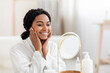 Facial Care. Attractive Black Woman Looking At MirrorAnd Touching Face