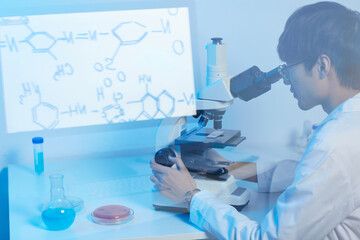 Serious focused modern Asian scientist in glasses sitting at desk in laboratory and using microscope while studying molecules