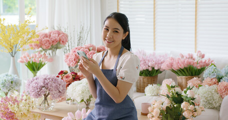 Wall Mural - Asia people young woman SME owner happy smile look at camera enjoy open flower shop sale order web page work at home office workspace. Loan money banking for social media commerce online store seller.