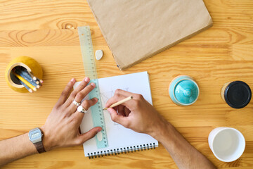 Aufkleber - Above shot of hands of multi-ethnic guy making sketch of new item of earthenware while sitting by wooden table in workshop