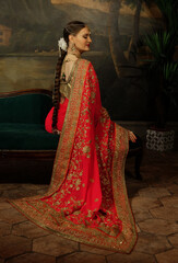 Charming woman is sitting on the sofa. Traditional Indian wedding sari and jewelry.