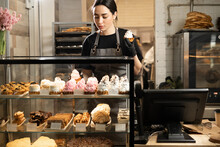 Handsome Woman Coffee Shop Employee Placing Pastry And Cake In Bakery Refrigerator Showcase At Cafe. Small Business, Part Time Job