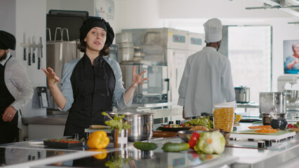 POV of professional cook making cooking show content with food in restaurant kitchen, filming vlog on camera. Authenic woman in uniform doing meal preparations for gastronomy program. Tripod shot.