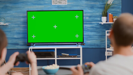 Canvas Print - Closeup of couple holding controllers playing action console games on green screen tv sitting on couch and eating popcorn. Young gamers spending free time gaming online on chroma key mockup display.