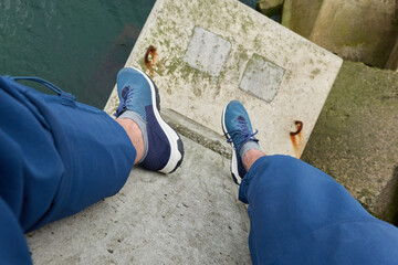 Wall Mural - Man sitting on breakwaters. Blue jeans, trekking boots. Sea water surface texture. Turquoise tones. Soft sunlight. Nature, wanderlust, sport, leisure activity themes. Top down view. Panoramic image