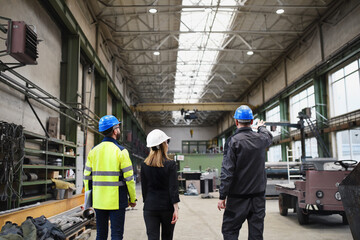 Wall Mural - Rear view of manager supervisors and industrial worker in uniform walking in large metal factory hall and talking.