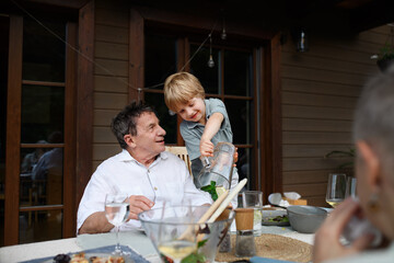 Little boy pouring lemonade to his grandfather during family celebration outside on patio.