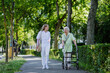 © Halfpoint - Caregiver with senior woman on walk with walker in park with shopping bag.