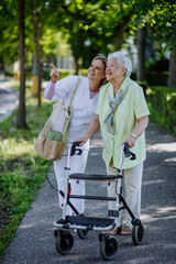 Wall Mural - Caregiver with senior woman on walk with walker in park with shopping bag.