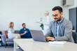 © bnenin - An adult businessman using a laptop, working while his colleagues sitting in the background.