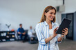 © bnenin - Smiling adult woman, looking at the tablet, using it while her colleagues sitting in the background.