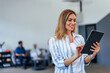 © bnenin - Side view of a businesswoman, holding and using a tablet while standing in the middle of the office.
