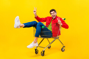 Poster - Full length body size view of attractive cheerful childish guy riding cart showing v-sign isolated on bright yellow color background