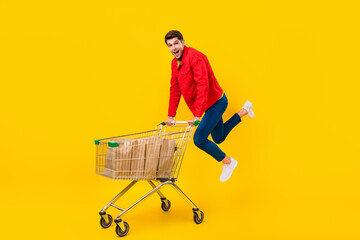 Poster - Full length body size view of attractive funny cheerful guy holding cart jumping isolated over bright yellow color background