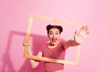 Wall Mural - Portrait of adorable laughing girl break through photograph reaching you isolated on pink color background