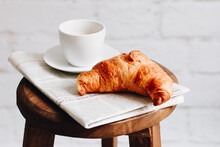 Breakfast Croissant, Cup Of Coffee And Newspaper On A Wooden Stool