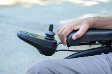 A Person With A Disability Operates A Wheelchair. Man Using Joystick To Drive Electric Wheelchair, Close Up. 