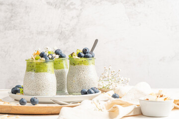 healthy breakfast chia pudding with kiwi, blueberries and coconut slices, three portions in glass ja