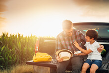 Father And Son Sits On Truck Trunk Outdoor On Field . They Enjoying Time Together