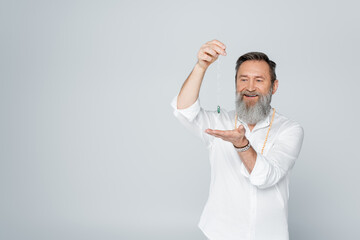 senior guru man smiling while meditating with dowsing pendulum isolated on grey.