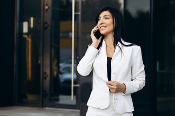 Business woman in white suit talking on the phone by the office building