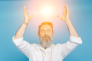 master guru meditating with closed eyes and raised hands near shining aura isolated on blue.