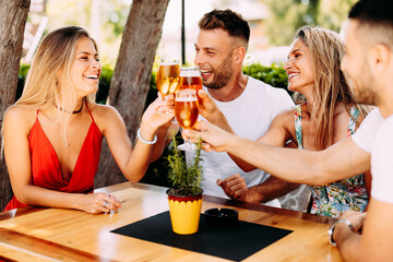 Wall Mural - Group of happy friends toasting with beer in the backyard at a wooden table. Selective focus on beer