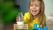 © Belkina Margarita - Close up of toy tractor delivers milk to little girl lying on floor. Happy child laughs and drinks milk from bottle with straw