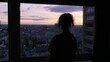 A woman watches the sunset from the window of her building, in Paris, France