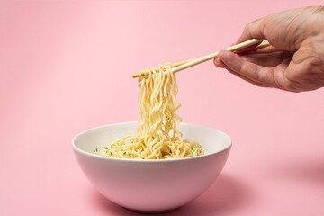 Sticker - Boiled instant noodles on a pink background. Hand takes noodles with chopsticks for food. Fast food. Modern food.