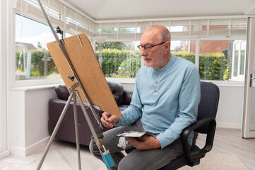 Wall Mural - Environmental portrait of a retired senior.  An artist painting with watercolours in his home studio.