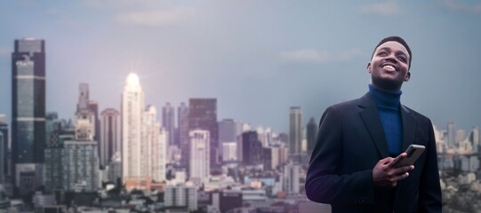 African businessman in a suit holds a smartphone with tall buildings in the capital in the background