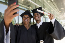 Happy College Graduates In Caps And Gowns Posing For Selfie