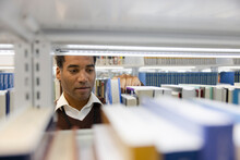 Male Librarian Retrieving Book From Shelf In Library