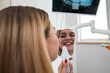 © Tania - a girl looking in the mirror at her white teeth while sitting in a chair at the dentist.