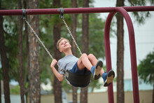 Young Handsome Teenage Boy Playing Alone On Playground Swings On Summer Vacations Sunny Day