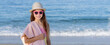 A teenage girl in a hat, with glasses and a towel on the background of the sea.