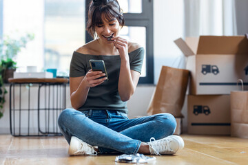 Young beautiful woman with mobile phone while eating a piece of chocolate sitting on the floor in her new house.